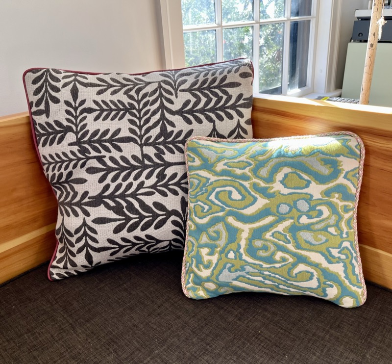 Two handmade throw pillows with piped edges, one in a black and white botanical leaf print and one in a blue and green ikat pattern